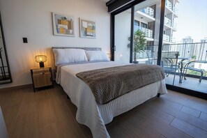 A modern bedroom with a large bed, a bedside table with a lamp, and a view of the city through a balcony. - Modern 2BR Apartment, Fully Equipped, Pool and Gym, (Panamá)
