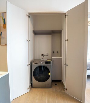 Een ruime wasruimte met een voorlader wasmachine, een klein kastje en een betegelde vloer.