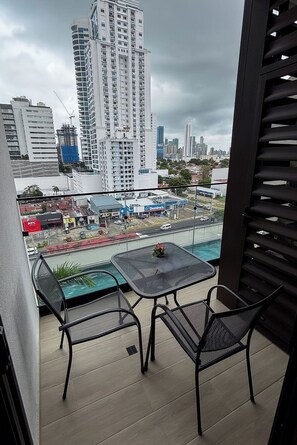 A balcony with a table and chairs, overlooking a cityscape with high-rise buildings and a KFC restaurant. - Modern 2BR Apartment, Fully Equipped, Pool and Gym, (Panamá)