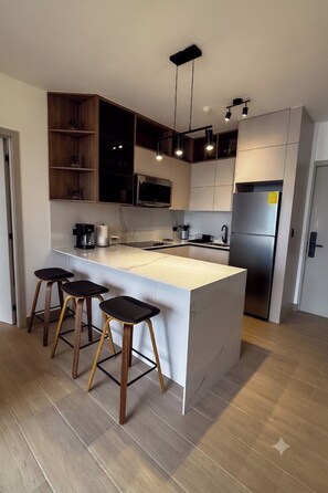 A modern kitchen with a central island, bar stools, a microwave, a refrigerator, and pendant lighting. - Modern 2BR Apartment, Fully Equipped, Pool and Gym, (Panamá)