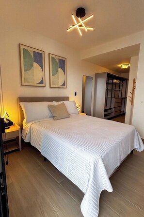 A bedroom with a bed, bedside lamps, abstract wall art, and a modern ceiling light fixture. - Modern 1BR with Balcony and Sofa Bed -4 guests (Panamá)