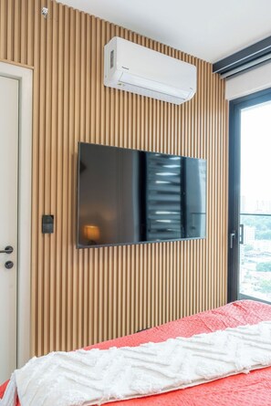 A hotel room with a mounted flat-screen TV, a sliding door, and a bed with a red and white blanket. - 2 bedrooms/2 bathrooms at The Hub, San Francisco PTY (Panamá)
