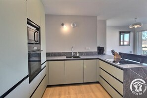 A modern kitchen with a built-in oven, a sink, and a black countertop. - Le Riva - FREHEL - Vacation Rental (FREHEL)