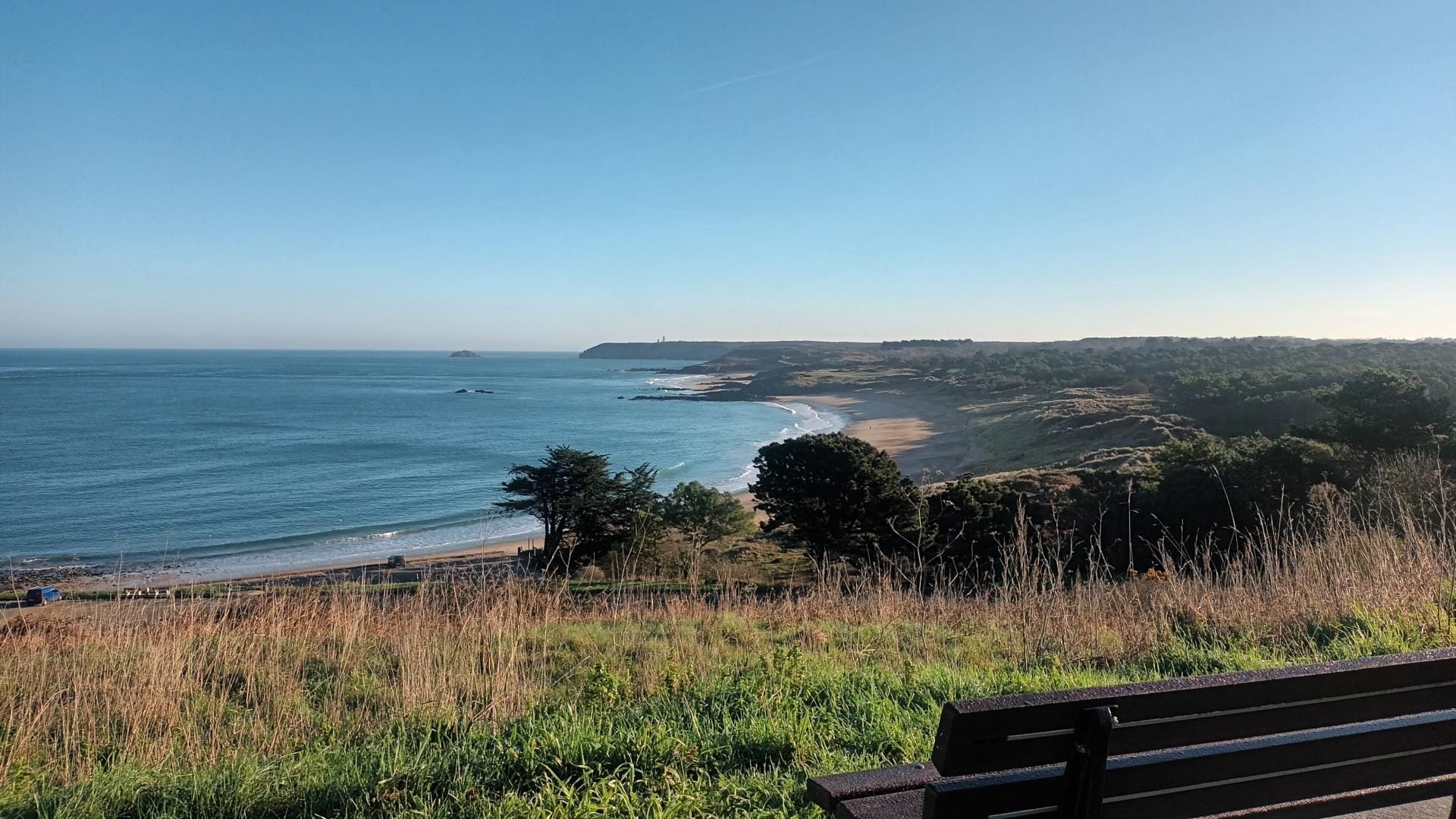 A coastal landscape with a bench overlooking a beach and ocean.