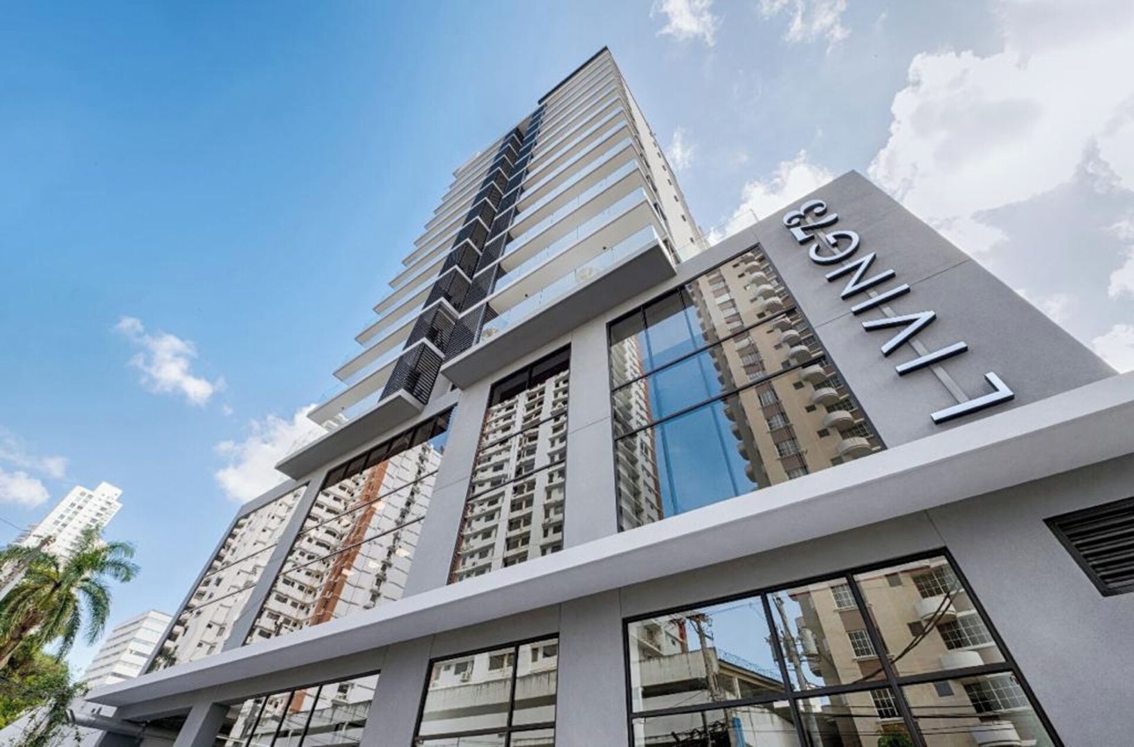 A modern high-rise building with a prominent 'LIVING' sign, featuring a sleek architectural design with reflective glass windows and a series of balconies.