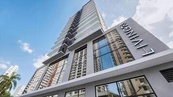 A modern high-rise building with a prominent 'LIVING' sign, featuring a sleek architectural design with reflective glass windows and a series of balconies.