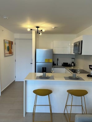 Cozinha moderna com armários brancos, eletrodomésticos de aço inoxidável e uma ilha central com banquetas.