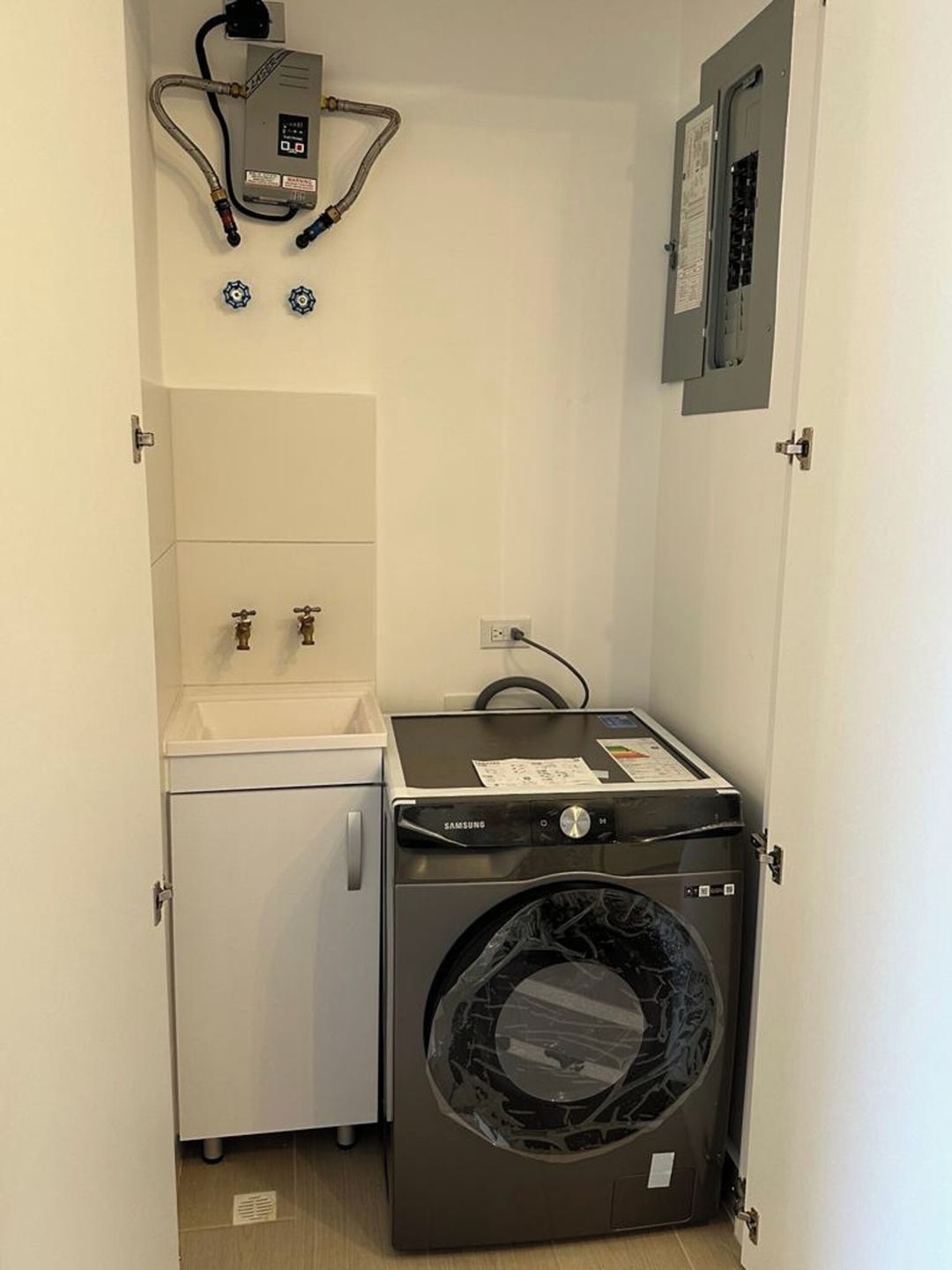 A compact laundry room with a washing machine, a small sink, and a water heater.