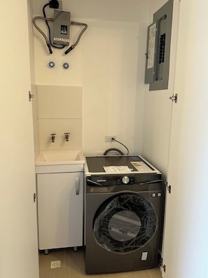 Uma lavanderia compacta com máquina de lavar, pia pequena e aquecedor de água.
