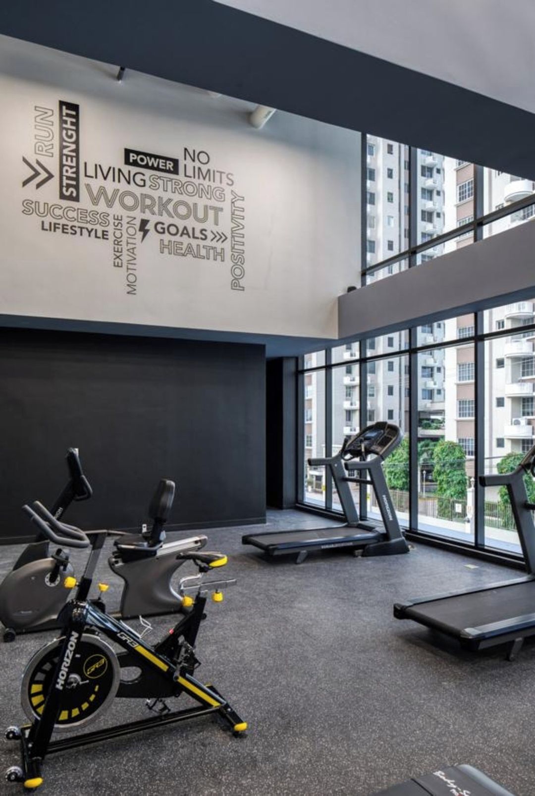A modern gym with exercise equipment, motivational wall art, and large windows offering a view of the city.