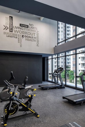 Academia moderna com equipamentos de ginástica, painel decorativo com mensagens motivacionais e amplas janelas com vista para a cidade.