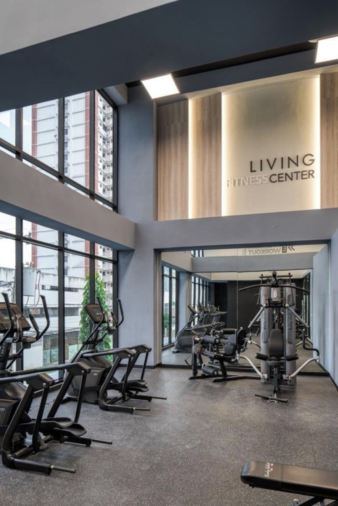 A gym with exercise equipment, large windows, and a sign reading 'LIVING FITNESS CENTER'.