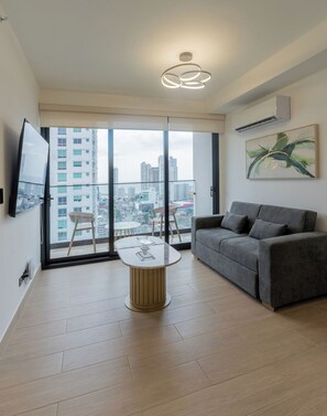 A modern living room with a grey sofa, a glass-top coffee table, and a city view through large windows. - 2BR/2BA at The Hub, San Francisco PTY (Panamá)