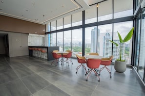 A modern office space with a large window, a round table with chairs, a potted plant, and a kitchenette area. - Hotel-Style Room at The Hub, San Francisco (Panamá)