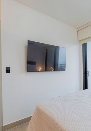 A room with a large wall-mounted TV, a door with a sliding glass window, and a bed with a textured white cover. - Hotel-Style Room at The Hub, San Francisco (Panamá)