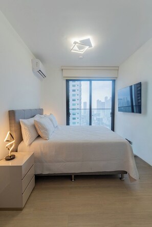A modern bedroom with a bed, nightstand, and a city view through the window. - Modern 1-Bedroom Apartment in The Hub / Pool / Gym / Upper Floor (Panamá)