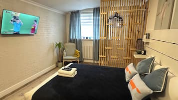 A modern bedroom with a bed, a TV mounted on the wall, a chair, a small table, and a decorative wooden partition.
