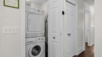 Une buanderie équipée d’un lave-linge et d’un sèche-linge superposés, d’une porte dotée d’un judas et d’un luminaire fixé au mur.