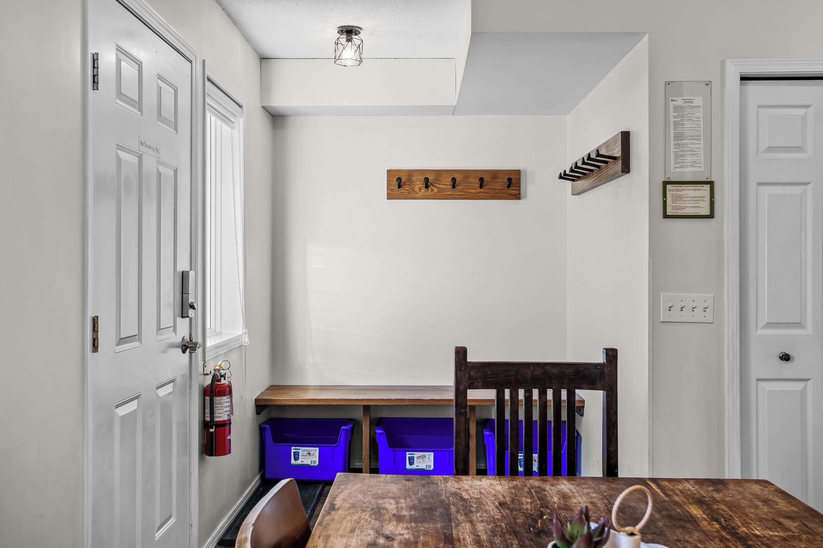 Une pièce comprenant une table en bois, une chaise, un extincteur et deux bacs de rangement bleus.