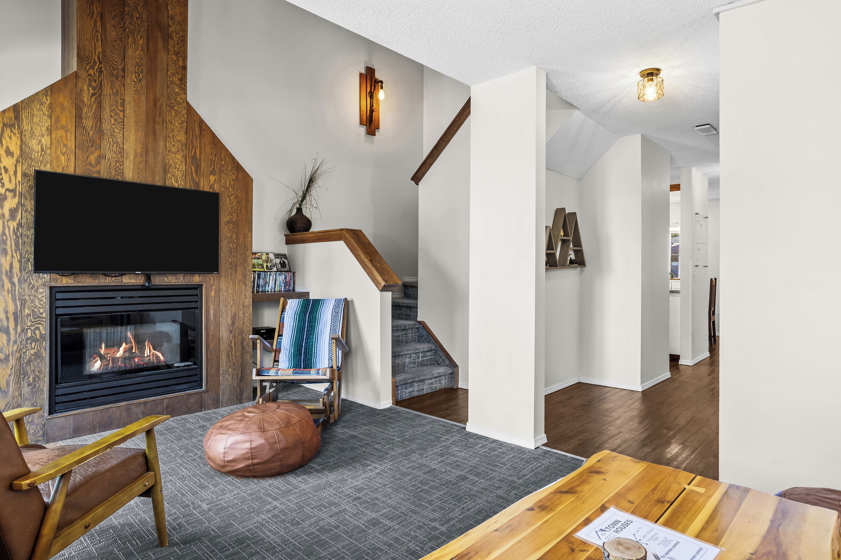 A modern living room with a fireplace, a television, a wooden accent wall, and a staircase.