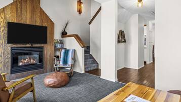 A modern living room with a fireplace, a television, a wooden accent wall, and a staircase.
