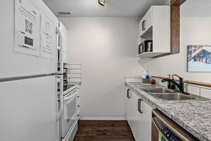 Ett kompakt kök med vita skåp, en inbyggd ugn, en diskmaskin och en diskho med en modern blandare.