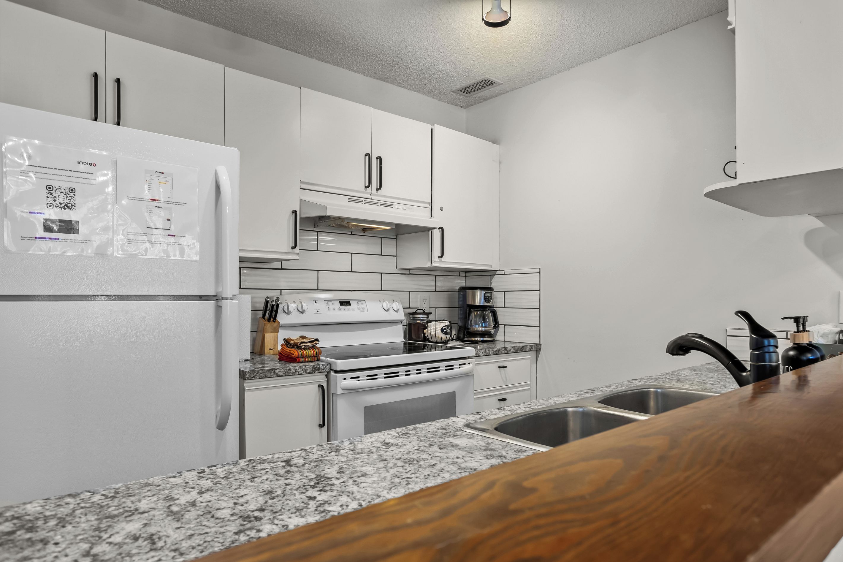 Une cuisine moderne avec des meubles blancs, un four encastré, une plaque de cuisson et un plan de travail en granit.