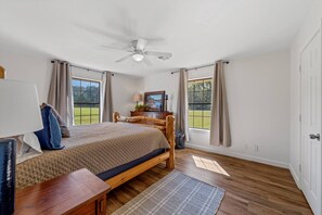 Ein Schlafzimmer mit einem Bett, einem Schreibtisch, einem Stuhl, einem Deckenventilator und großen Fenstern.