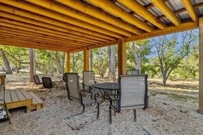 Een overdekt terras buiten, met houten balken, een tafel, stoelen en een barbecuehoek.