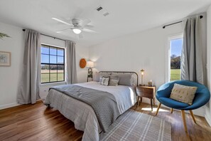 Een slaapkamer met een bed, een stoel, een nachtkastje, een lamp en een plafondventilator.
