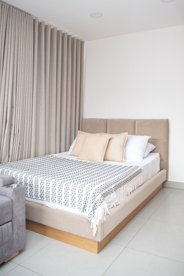 Een slaapkamer met een bed, gordijnen, een stoel en een betegelde vloer.