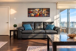Un salon moderne avec un canapé en cuir, une table basse et une vue sur la ville grâce à de grandes fenêtres.