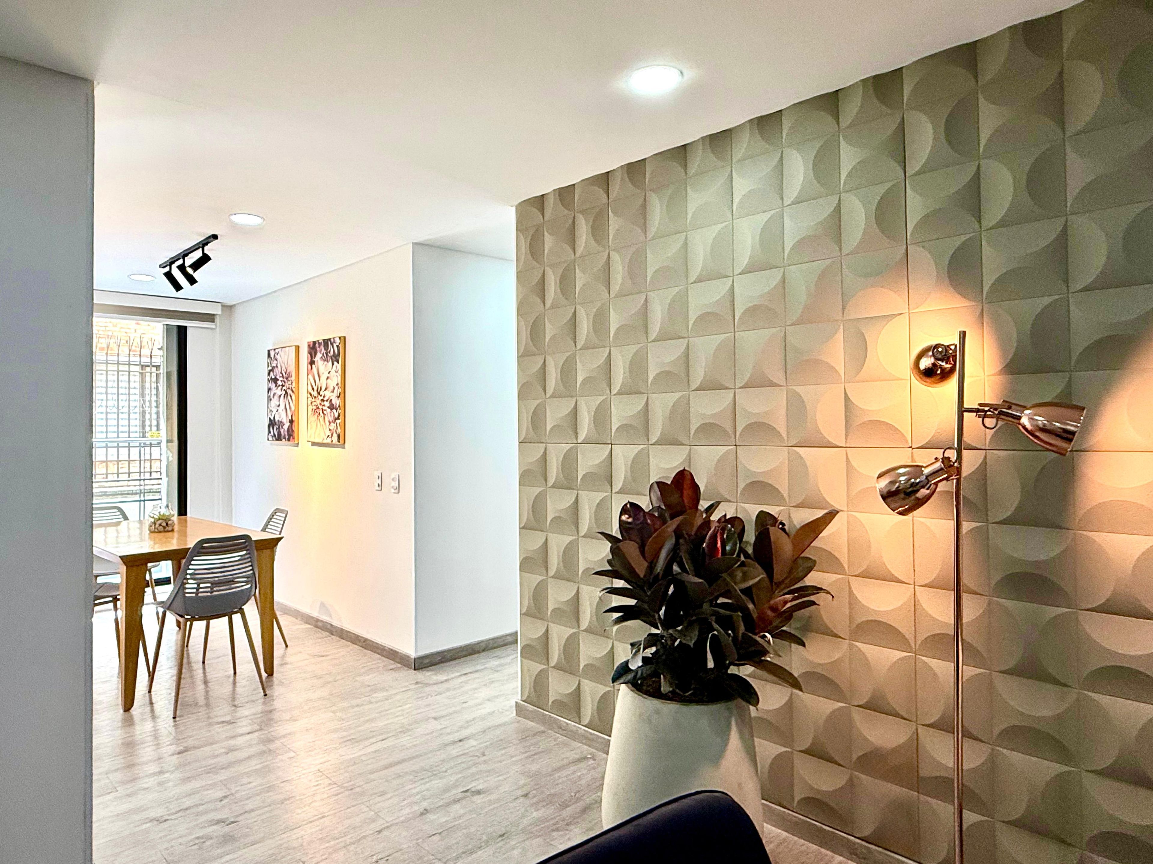 Una sala de estar moderna con comedor, que presenta una pared con diseño geométrico, una planta en maceta y una lámpara fijada al techo.