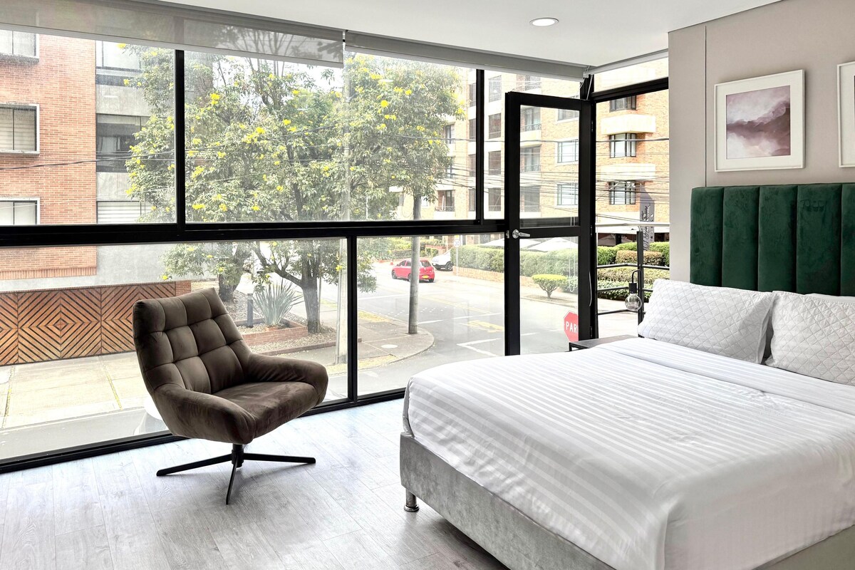 Une chambre d’hôtel avec une grande fenêtre, un lit, une chaise et une vue sur la rue.
