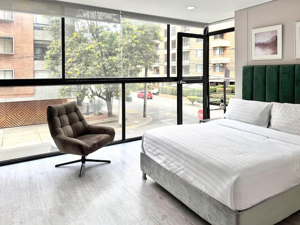 A hotel room with a large window, a bed, a chair, and a view of the street. - Espacioya By Mario Rental (Kappadocia) (Bogotá)