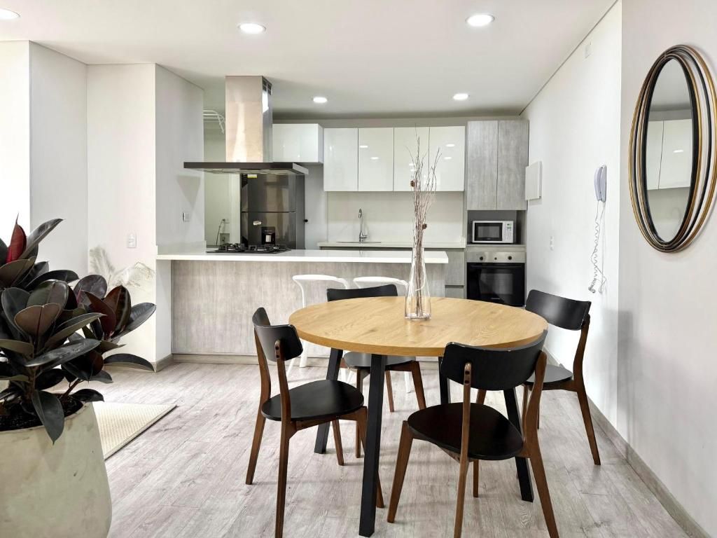 Una cocina moderna con armarios blancos, una isla central y un comedor con una mesa redonda y sillas.