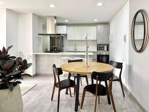 A modern kitchen with white cabinets, a central island, and a dining area with a round table and chairs. - Espacioya By Mario Rental (Kappadocia) (Bogotá)