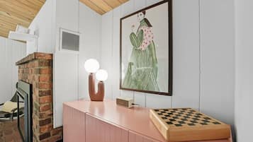Una habitación con chimenea de ladrillo, un armario rosa, una obra de arte enmarcada y un tablero de ajedrez.