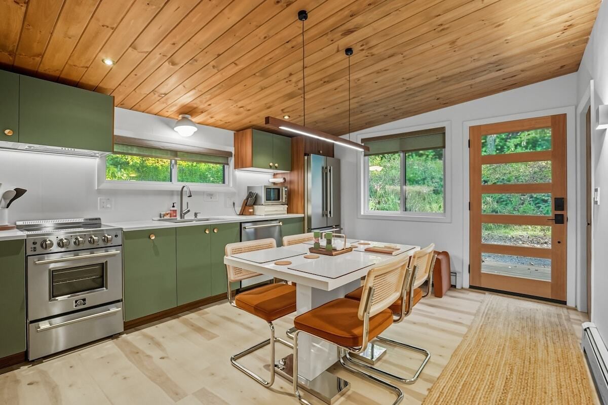 A modern kitchen with green cabinets, stainless steel appliances, and a dining area with a white table and brown chairs.