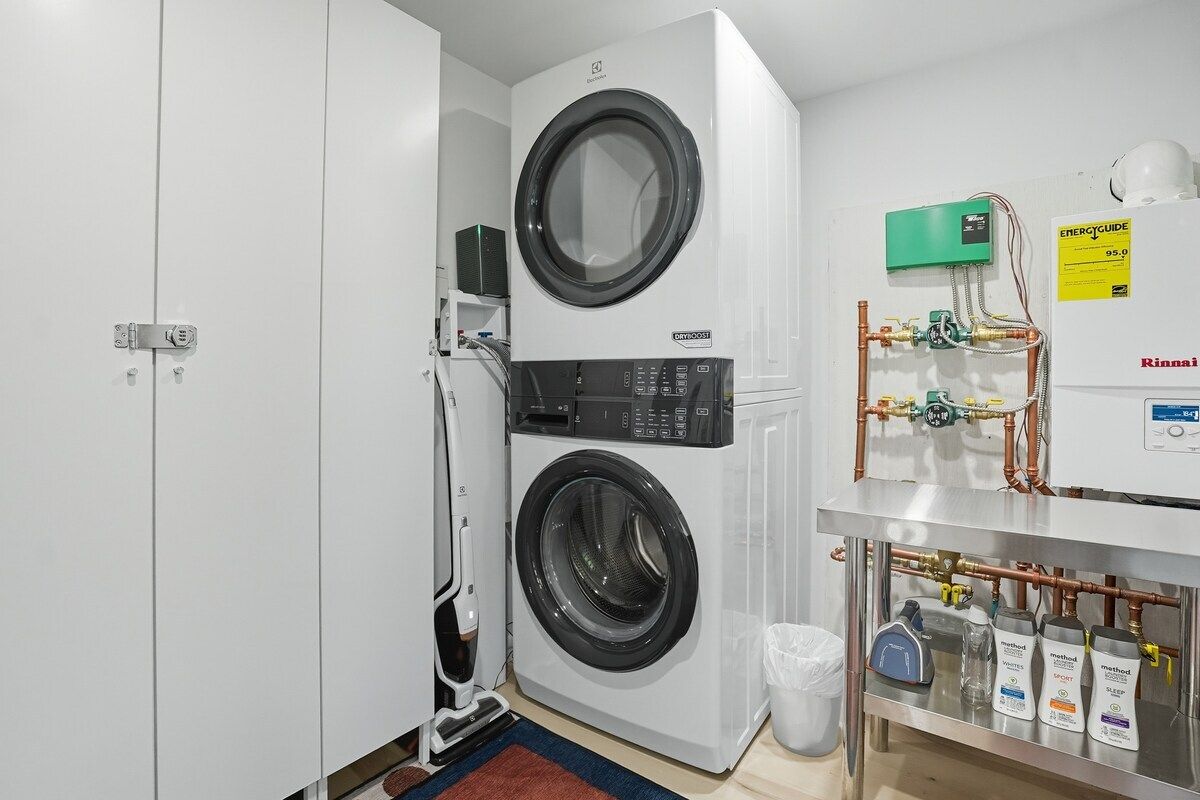 A laundry room with two stacked front-loading washing machines, a water heater, and various plumbing fixtures.