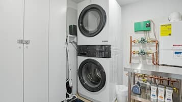 A laundry room with two stacked front-loading washing machines, a water heater, and various plumbing fixtures.