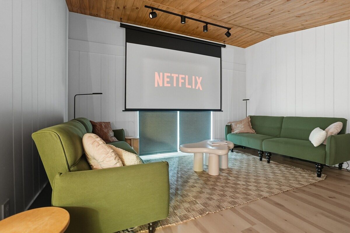 A modern living room with two green sofas, a coffee table, and a large screen displaying 'NETFLIX'.