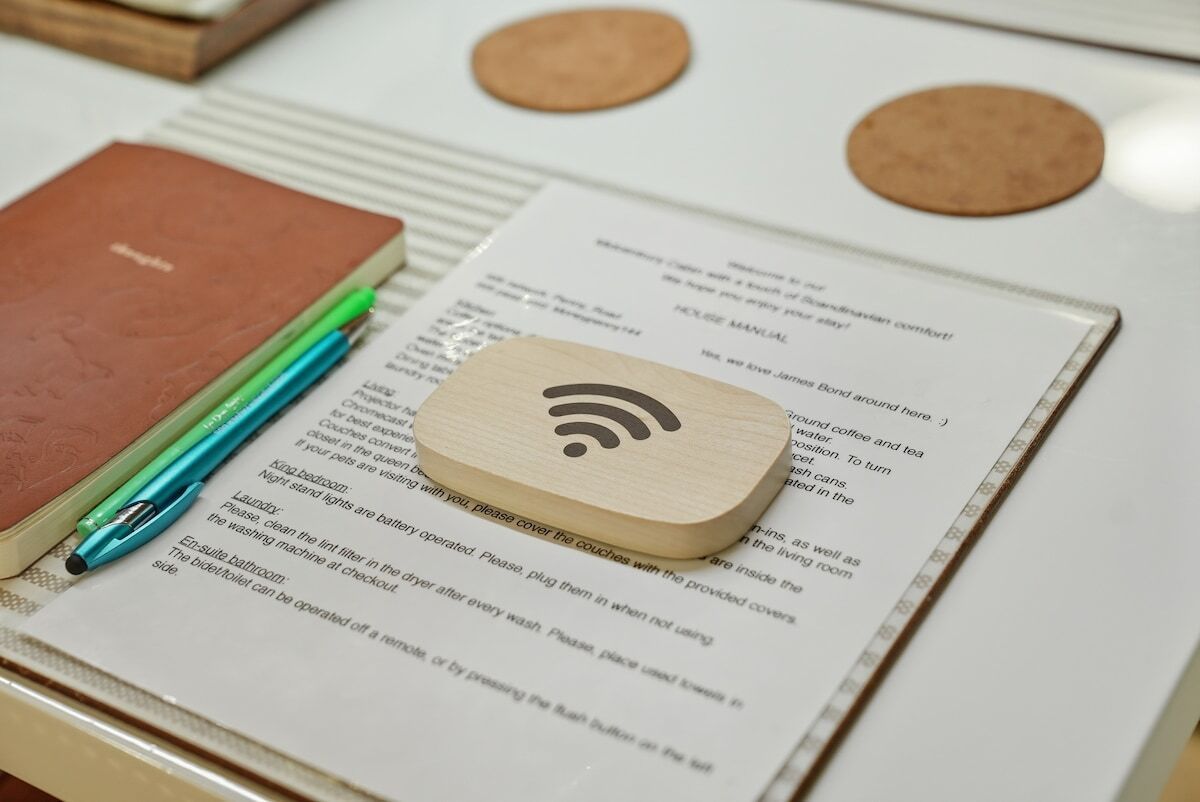 Un letrero de madera con el símbolo de Wi-Fi, una libreta y un bolígrafo sobre una mesa con un documento impreso.