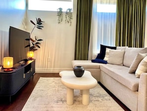A living room with a sofa, a coffee table, a TV stand, and a decorative plant. - Steps to Yale! DWTN 2BR King Beds • Free Parking • Gym (New Haven)