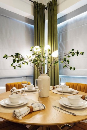 Et spisebord dækket til fire personer med hvide tallerkener, glas og en vase med grene.