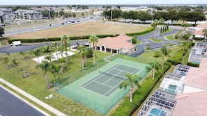 A residential area with a tennis court, a swimming pool, and a road with vehicles. - Sundrop Oasis ☀️ | Remodeled 3-Bedroom Private Pool Villa Near Disney (Davenport)