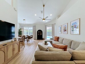 A spacious living area with a flat-screen TV, a ceiling fan, a dining table with chairs, and a sofa with cushions. - Sundrop Oasis ☀️ | Remodeled 3-Bedroom Private Pool Villa Near Disney (Davenport)