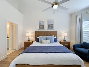 Quarto com cama, duas mesas de cabeceira com luminárias, ventilador de teto e duas molduras na parede.
