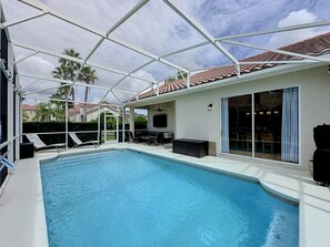A covered outdoor swimming pool with a patio area, a television, and a sliding glass door leading to an indoor space. - Sundrop Oasis ☀️ | Remodeled 3-Bedroom Private Pool Villa Near Disney (Davenport)