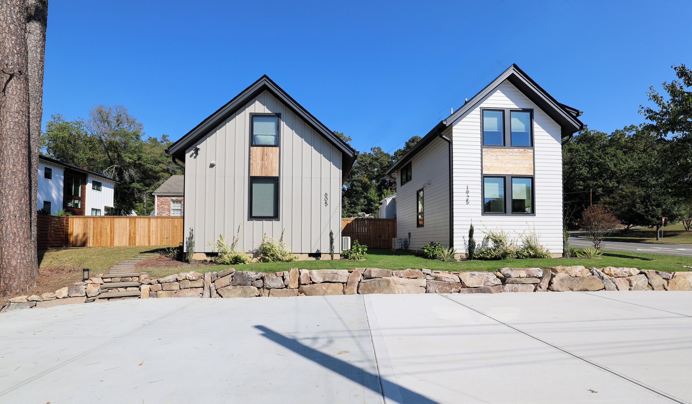 Two modern houses with gabled roofs, a stone wall in the foreground, and a clear blue sky.